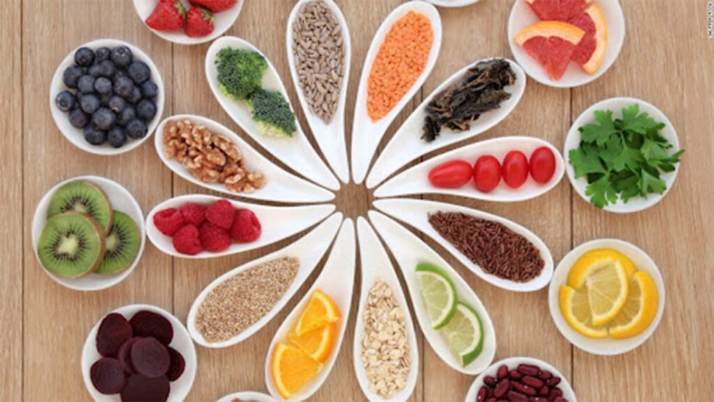 Naturopathic Remedies for IBS Relief 3 Remedies for IBS Relief: Assorted fruits, vegetables, nuts, seeds, and herbs in white bowls forming a circular pattern on a wooden table.