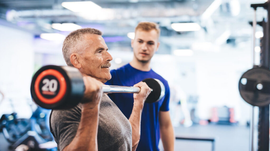 Naturopathic Remedies for IBS Relief 7 Remedies for IBS Relief: Elderly man exercising with dumbbells in gym, assisted by trainer; promotes digestive health through physical activity.