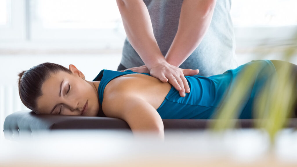 Natural Pain Relief: A woman relaxes during a massage therapy session in a calming spa environment, receiving targeted back treatment.