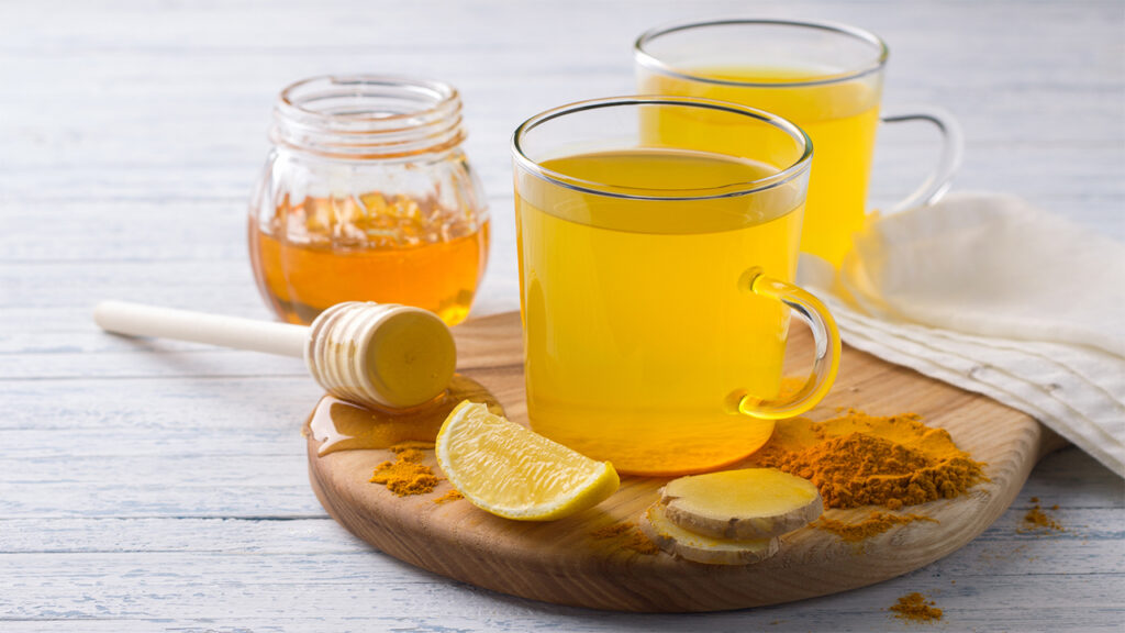 Remedies for IBS Relief: Turmeric Tea with Honey and Lemon in mugs on a board, with ginger slices, turmeric powder, and honey dipper